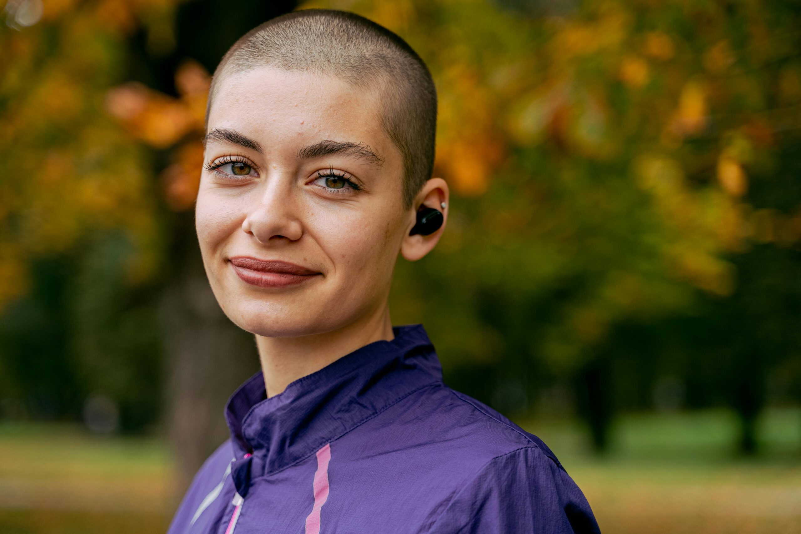 Portrait of a woman with a buzzcut wearing earbuds outdoors in autumn
